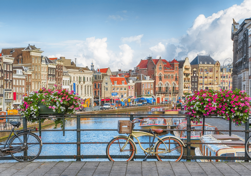 Colorful historic city buildings along a canal with a bicycle and boats in the foreground.